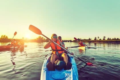A blonde woman and a Caucasian man are in a blue kayak. A child sits on the woman's lap, holding a paddle.