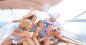 A mother, father, and two daughters laugh and smile together while wearing sunglasses on a sunny day aboard a boat.