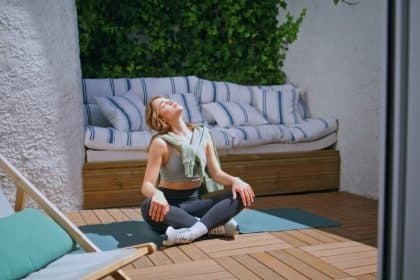 A young mom sits on her patio on a yoga mat in activewear as she gazes up at the sun for a moment of meditation.