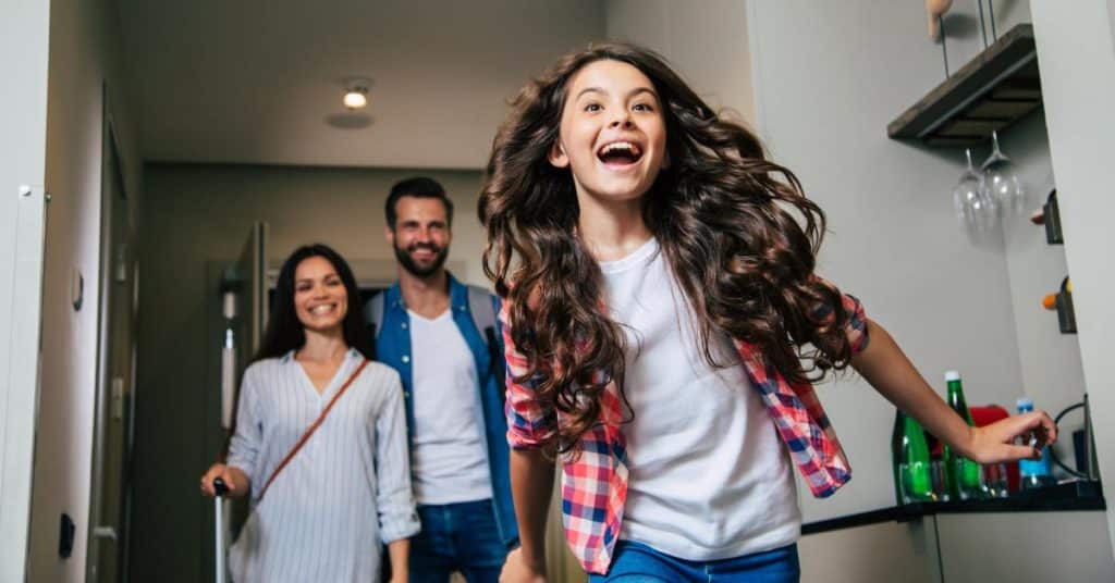 A child excitedly running into a hotel room while their parents follow behind them, bringing in the luggage.