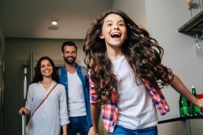 A child excitedly running into a hotel room while their parents follow behind them, bringing in the luggage.