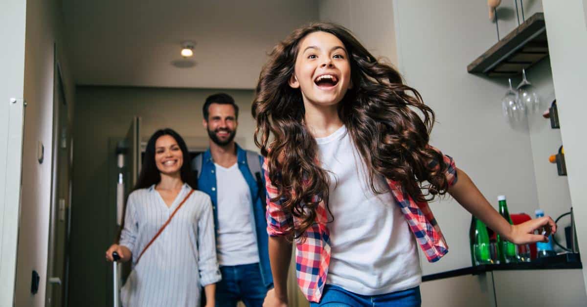 A child excitedly running into a hotel room while their parents follow behind them, bringing in the luggage.