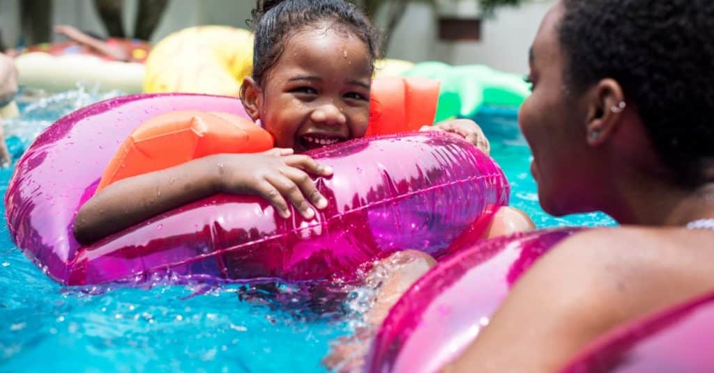 A close-up of a mother and daughter floating in a swimming pool while sitting in colorful inflatable tubes.