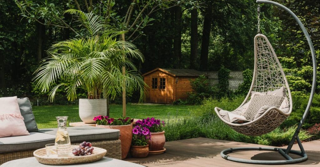A well-decorated backyard of a home. There is a hanging chair, a couch with ottomans, and potted plants laid out.