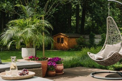 A well-decorated backyard of a home. There is a hanging chair, a couch with ottomans, and potted plants laid out.