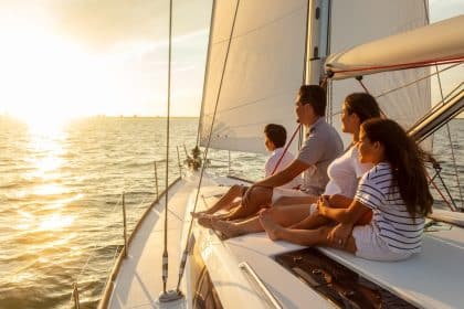 Family sitting on sailboat at sunset, looking toward horizon over calm sea, enjoying warm light and peaceful atmosphere.