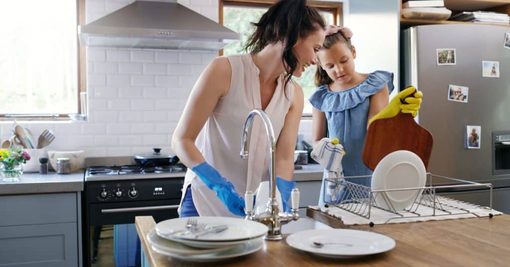 A mom and daughter wearing rubber gloves cleaning dishes in a residential kitchen during the daytime.