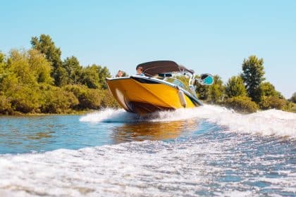 A yellow speedboat cuts across a lake at high speed, creating a foamy wake as passengers enjoy a sunny day on the water.