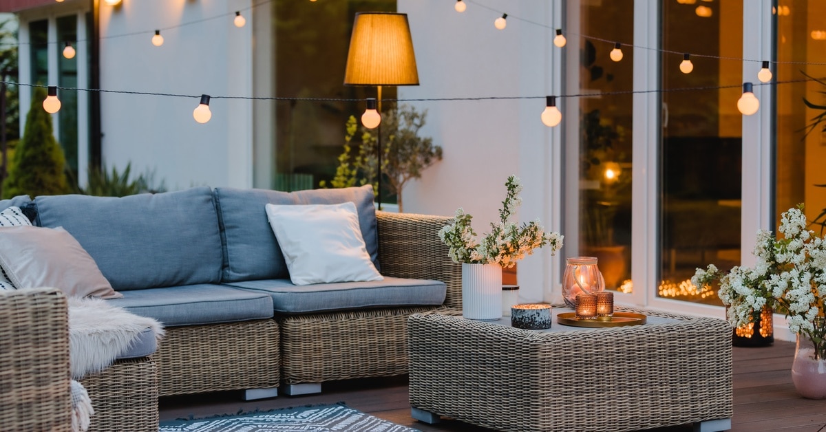 A close-up of an outdoor living space with string lights, an outdoor sofa, a coffee table, cushions, plants, and candles.