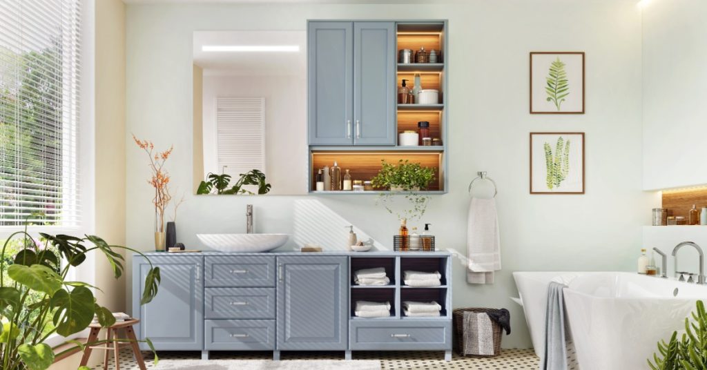 Airy bathroom features blue-gray vanities, a white soaking tub, botanical artwork, folded towels, and leafy plants.