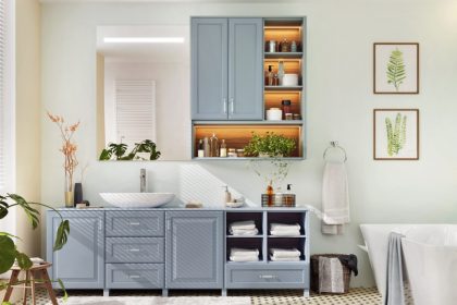 Airy bathroom features blue-gray vanities, a white soaking tub, botanical artwork, folded towels, and leafy plants.