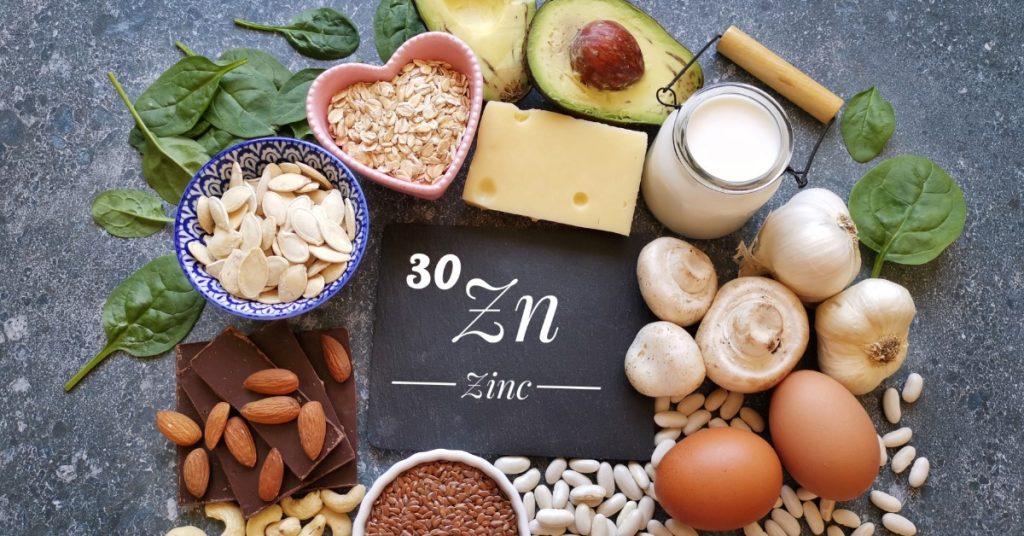 A chalkboard that contains the periodic symbol for zinc surrounded by foods with zinc, including eggs, mushrooms, and nuts.