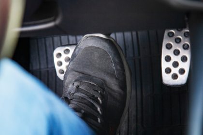 A person in the driver’s seat of a car wearing a black shoe and blue pants. The driver places a foot on the brakes.